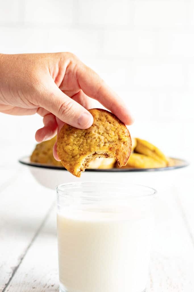 hand holding banana muffin top and dipping it in glass of milk