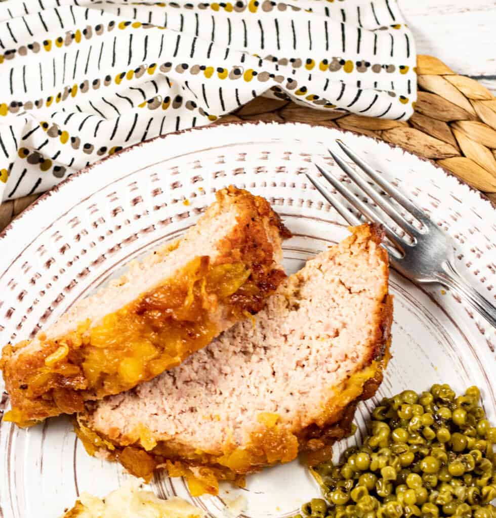 slices of Amish ham loaf on a plate with peas and mashed potatoes