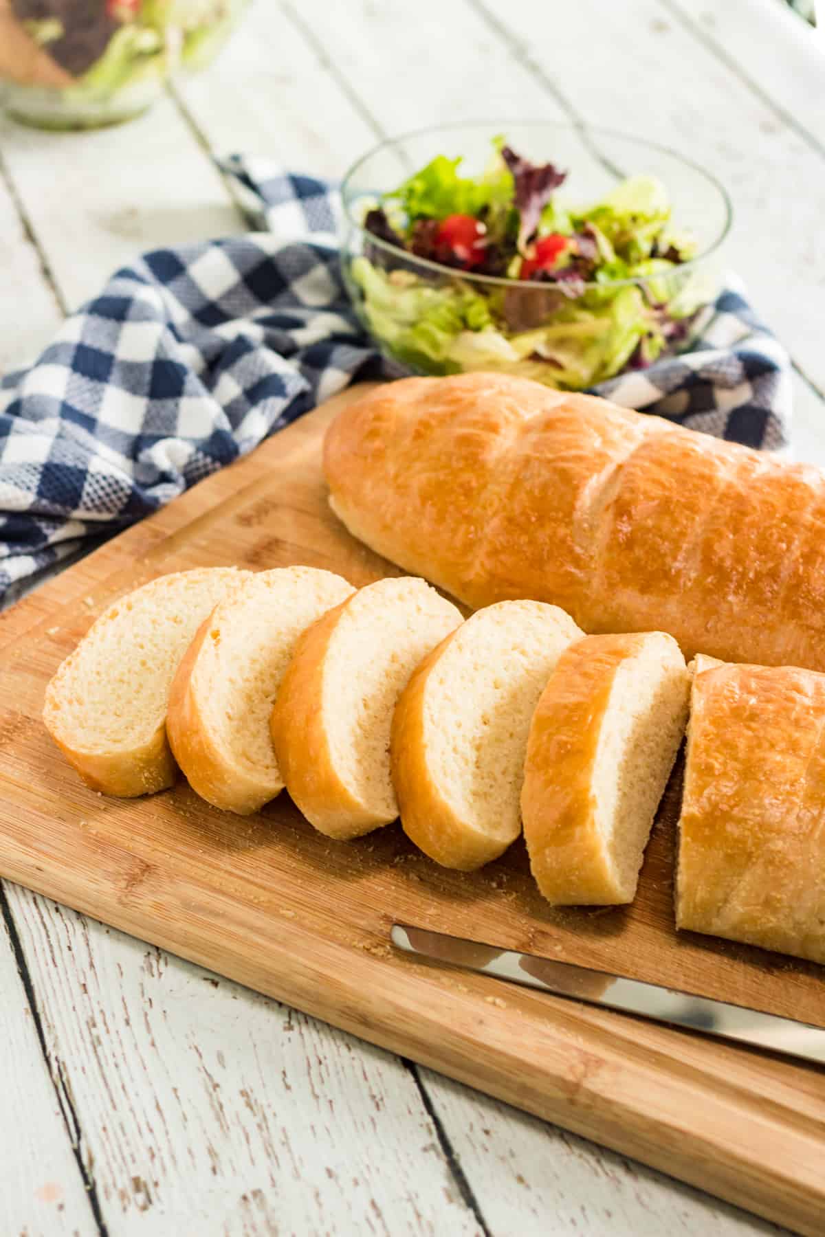 whole loaf french bread and sliced french bread on cutting board with blue checked napkin