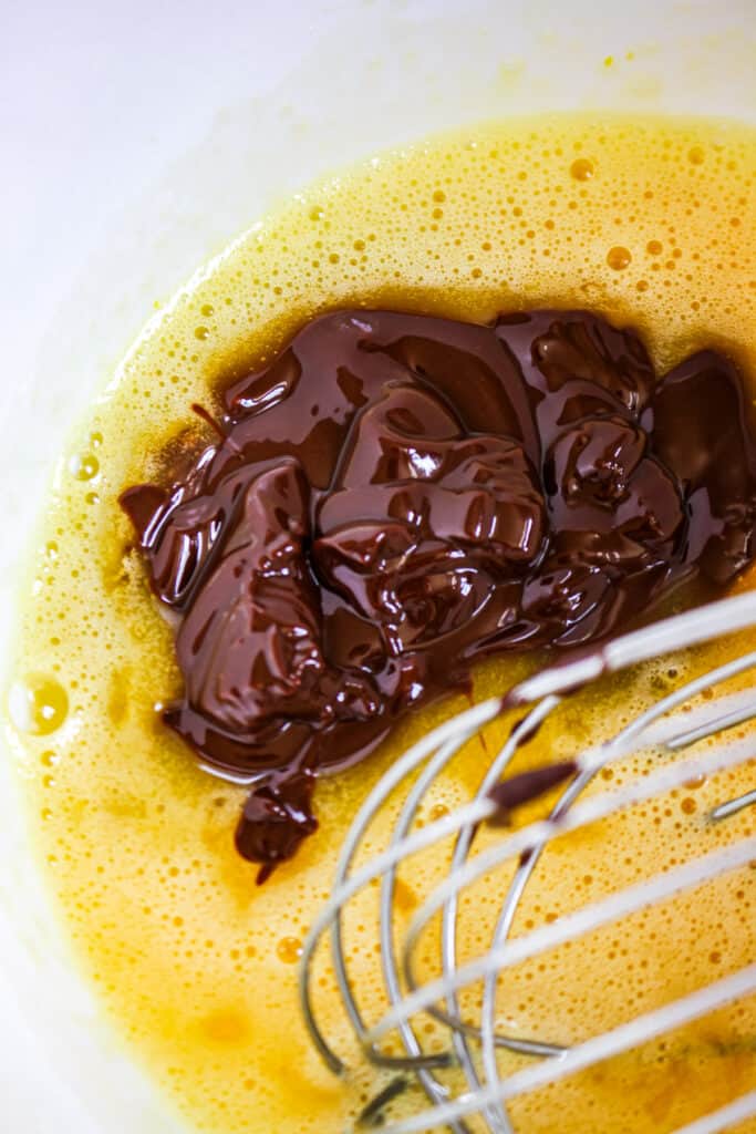 adding melted chocolate to eggs