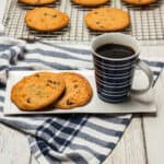 butterscotch cookies on a cooling rack with two cookies on a white plate and a blue cup with coffee.