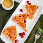 three slices of cranberry cake on a white plate with a ramkin of warm butter sauce