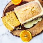 sliced orange loaf cake on wood tray, arranged with orange slices.